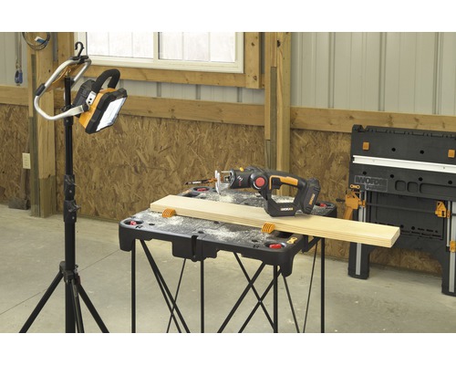 Werkbank mit Stichsäge, Holzstück und Stativleuchte in heller Werkstatt