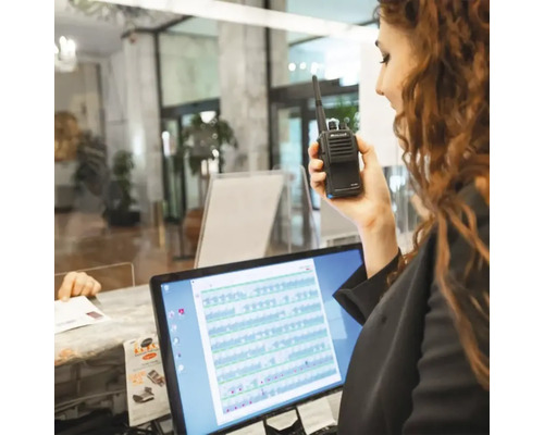 Frau hält ein Midland Funkgerät vor einem Computer.