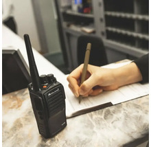 Ein Funkgerät der Marke Midland neben einer Person, die mit einem Stift auf Papier schreibt.