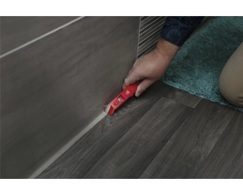 Handwerker entfernt Silikonfugen mit einem Fugenkratzer von Fliesen und Boden.