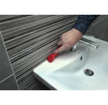 Eine Person entfernt Dichtungsmasse mit einem Fugenkratzer von einem Waschbecken