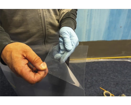 Eine Person mit Handschuhen hält eine transparente Schutzfolie.