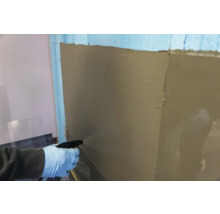 Eine Person befeuchtet eine Wand mit einer Sprühflasche, auf der bereits Putz aufgetragen wurde.