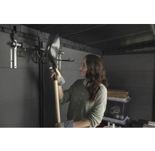 Frau hält eine Schaufel in einem Gartenschuppen mit Werkzeugaufhängungssystem