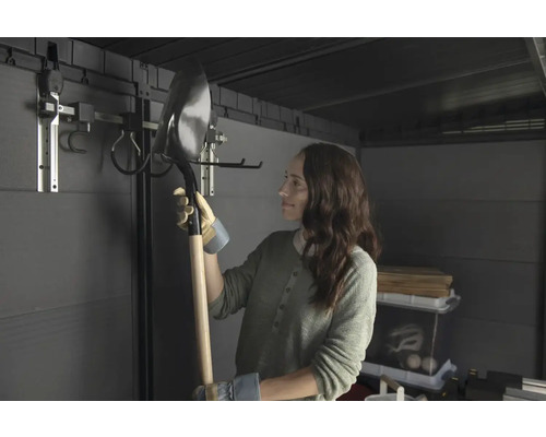 Frau hält eine Schaufel in einem Gartenschuppen mit Werkzeugaufhängungssystem