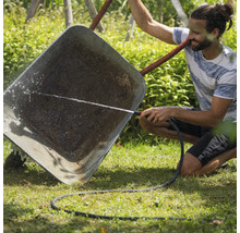 Ein Mann reinigt eine Schubkarre mit einem Gartenschlauch im Garten.