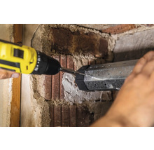 Eine Person befestigt ein Metallelement mit einem Akkuschrauber an einer Ziegelwand.