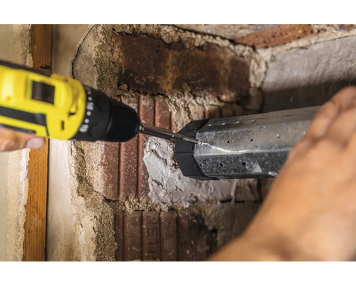 Eine Person befestigt ein Metallelement mit einem Akkuschrauber an einer Ziegelwand.