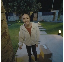 Frau lächelt vor ihrem Haus, mit einem Paket auf dem Boden