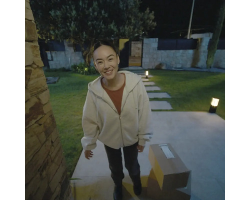 Frau lächelt vor ihrem Haus, mit einem Paket auf dem Boden