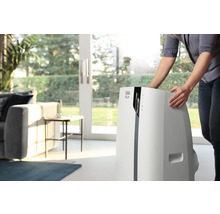 Frau positioniert ein mobiles DeLonghi Klimagerät im Wohnzimmer.