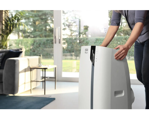 Frau positioniert ein mobiles DeLonghi Klimagerät im Wohnzimmer.