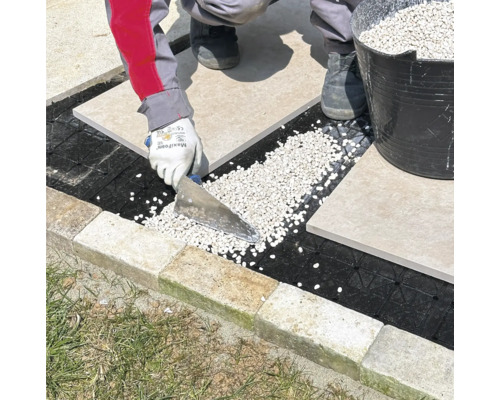 Verlegung von Terrassenplatten auf einem Kiesbett mit einem Spatel.