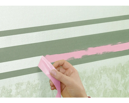 Eine Person entfernt Klebeband von einer Wand mit gemalten Streifen.