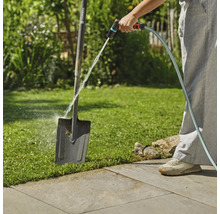 Gartenszene mit Person, die einen Spaten mit einem Wasserschlauch reinigt