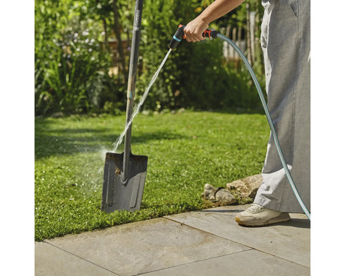 Gartenszene mit Person, die einen Spaten mit einem Wasserschlauch reinigt