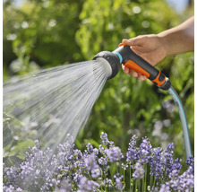 Eine Hand hält einen Gartenschlauch mit Brausekopf, der Wasser auf Blumen sprüht.