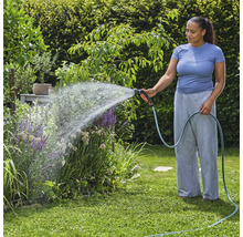 Frau bewässert Gartenpflanzen mit einem Gartenschlauch und einer Spritzpistole.