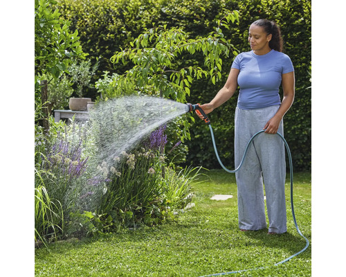 Frau bewässert Gartenpflanzen mit einem Gartenschlauch und einer Spritzpistole.