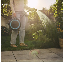 Frau gießt Pflanzen mit Schlauchaufroller im Garten.