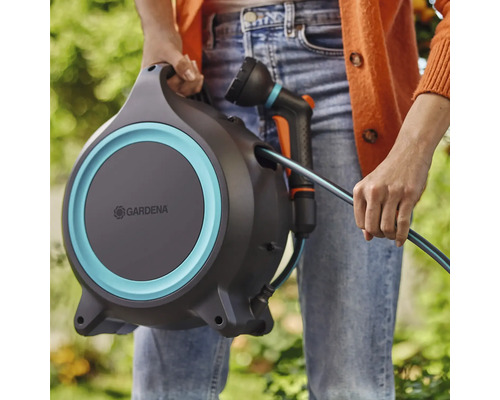Eine Person hält eine Gardena Schlauchbox mit Gartenschlauch und Spritze.