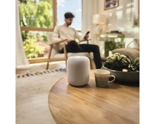 Intelligenter Lautsprecher auf einem runden Holztisch in einem Wohnzimmer