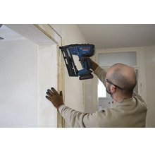 Ein Handwerker befestigt mit einem Akku-Nagler eine Leiste an einer Türzarge.