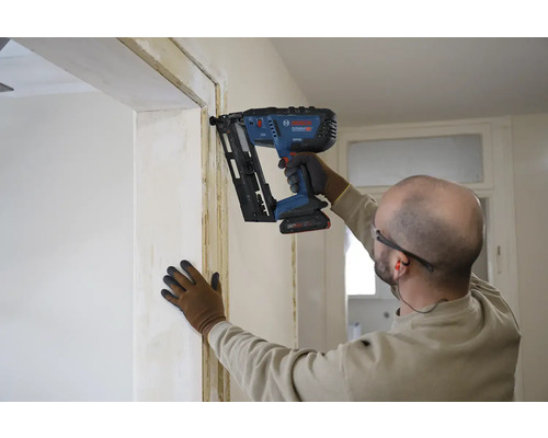Ein Handwerker befestigt mit einem Akku-Nagler eine Leiste an einer Türzarge.
