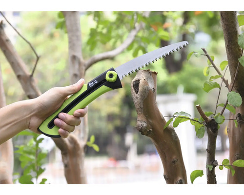 Eine Hand hält eine Astsäge beim Schneiden eines Astes.