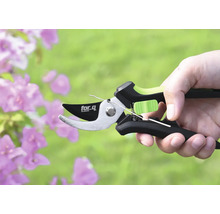 Eine Astschere der Marke for.q in einer Hand vor Blumen