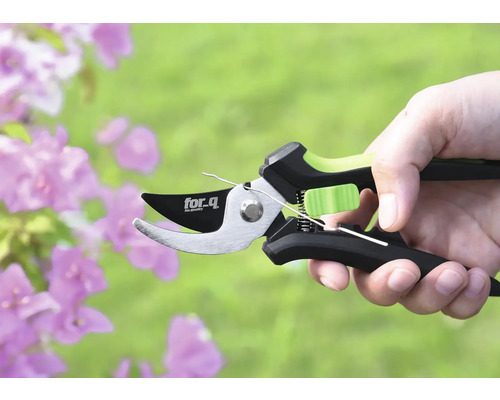 Eine Astschere der Marke for.q in einer Hand vor Blumen