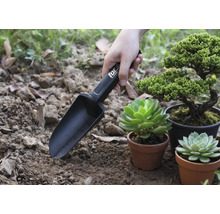 Gartenschaufel mit Markierungen im Einsatz neben Pflanzen in Töpfen.