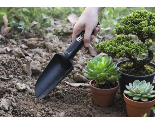 Gartenschaufel mit Markierungen im Einsatz neben Pflanzen in Töpfen.