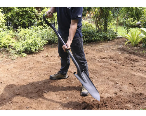 Mann hält Spaten im Garten.