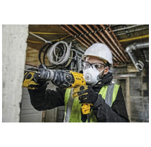 Ein Mann mit Schutzhelm, Schutzbrille und Atemschutzmaske bohrt mit einer gelben Bohrmaschine in eine Wand.