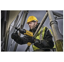 Ein Bauarbeiter bohrt mit einer Bohrmaschine ein Loch in eine Wand, während er auf einem Gerüst steht.