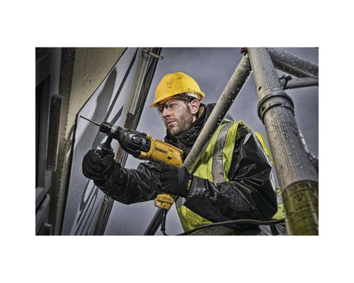 Ein Bauarbeiter bohrt mit einer Bohrmaschine ein Loch in eine Wand, während er auf einem Gerüst steht.