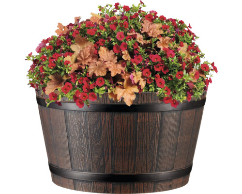 Blumenarrangement mit roten Blüten und Zierblättern in einem Holzfass