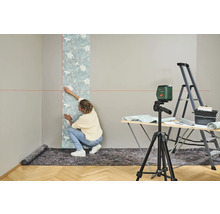 Frau tapeziert Wand mit Wasserwaage, Leiter und Tapeziertisch