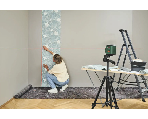 Frau tapeziert Wand mit Wasserwaage, Leiter und Tapeziertisch