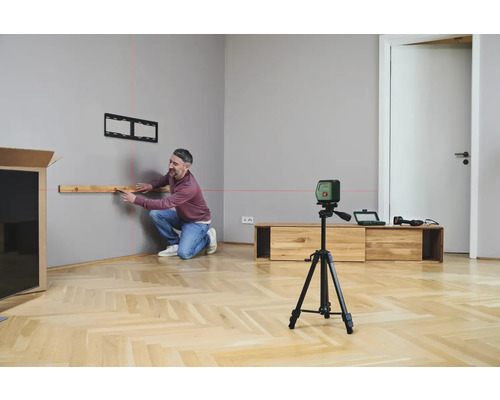 Mann montiert TV-Halterung mit Kreuzlinienlaser