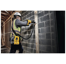 Ein Bauarbeiter bohrt mit einer Bohrmaschine und Staubabsaugung in eine Wand.