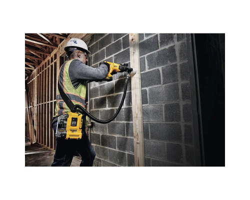 Ein Bauarbeiter bohrt mit einer Bohrmaschine und Staubabsaugung in eine Wand.