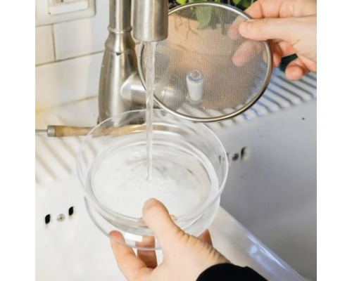 Eine Person wäscht einen Kaltbrühkaffee-Maker unter einem Wasserhahn.