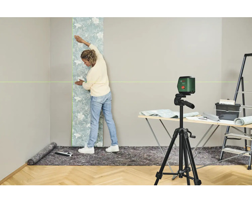 Frau bringt Tapete mit Laserwasserwaage an Wand an