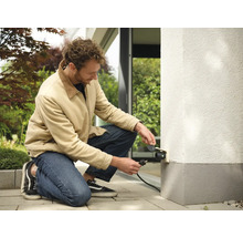 Mann schließt Außensteckdose an Hauswand an