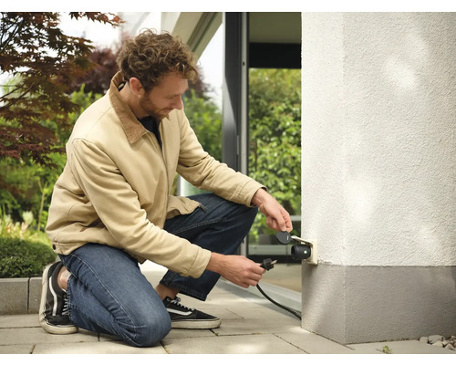 Mann schließt Außensteckdose an Hauswand an