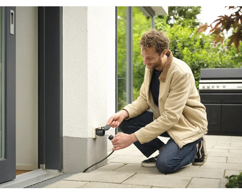 Mann schließt Stecker an Außensteckdose an