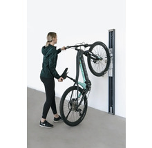 Frau hängt ein E-Mountainbike an einer Wandhalterung auf.