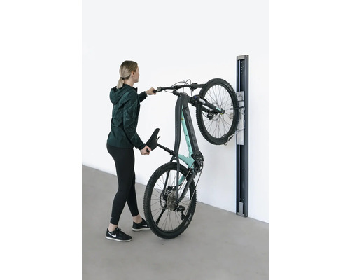 Frau hängt ein E-Mountainbike an einer Wandhalterung auf.